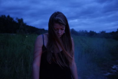 Young woman standing on grassy field against cloudy sky at dusk