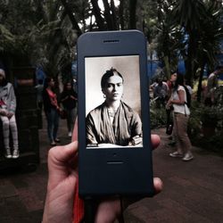 Midsection of man holding mobile phone while sitting on tree