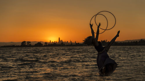 Silhouette woman by sea against sky during sunset
