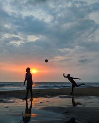 Silhouette people playing with ball at beach against sky during sunset