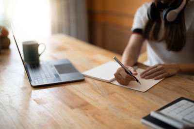 Midsection of woman writing in book on table