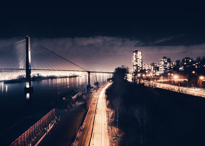 Illuminated bridge over river against sky at night