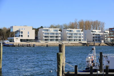 Buildings by sea against clear blue sky