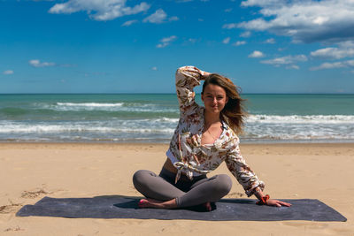 Rear view of woman sitting at beach against sky