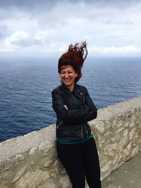 Smiling woman standing by retaining wall with sea in background