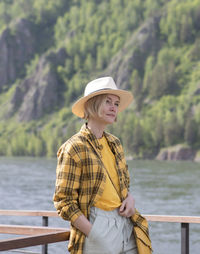 Side view of woman wearing hat standing against lake