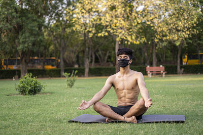 Full length of shirtless man sitting in park