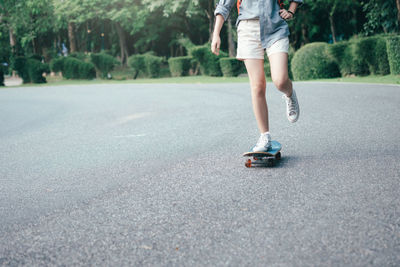 Low section of woman skateboarding on road