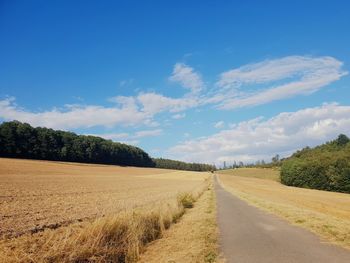 Empty road amidst field against sky