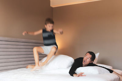 Playful kid in blurred motion jumping on a bed while playing with his father at home.