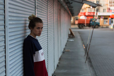 Young woman looking away while standing against shutter