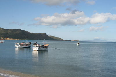 Boats sailing in sea against cloudy sky