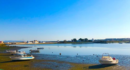 Boats moored at harbor against clear blue sky