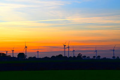 Scenic view of silhouette field with windmills  against sky during sunset