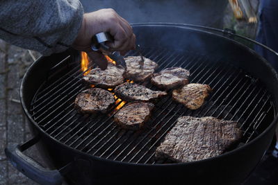 Cropped hand of man preparing meat on barbecue grill