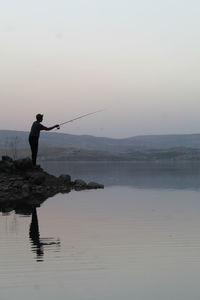 Man fishing in sea against sky