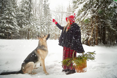 Rear view of woman with dog on snow covered field