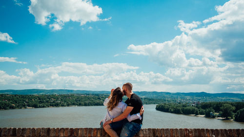 Woman sitting on retaining wall against sky