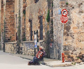 Man sitting on wall by road against building