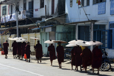 Monks walking on road by buildings during sunny day
