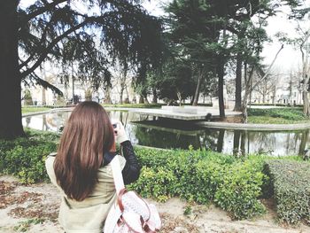 Rear view of woman photographing pond at public park