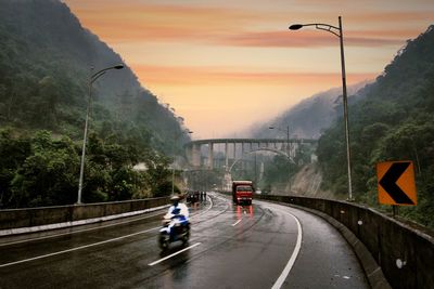 Vehicles on road against sky during sunset