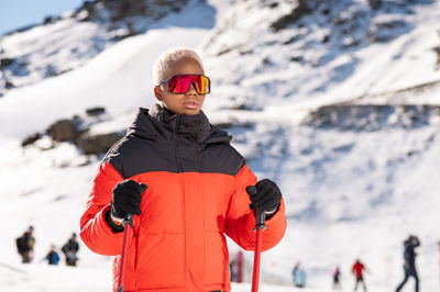 Una mujer afroamericana con bastones de esquí de pie en una montaña nevada durante el invierno