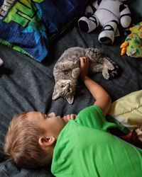 High angle view of boy stroking cat on bed at home