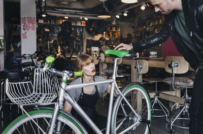 Female mechanic analyzing bicycle while talking to male customer in repair shop