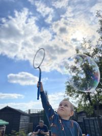 Portrait of boy looking at bubbles against sky