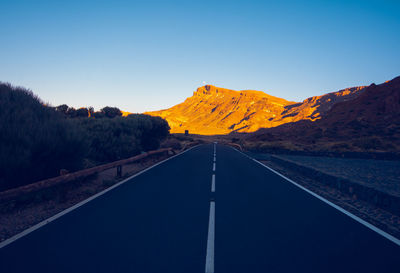 Empty road along landscape against clear blue sky