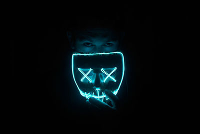 Portrait of man holding illuminated mask against black background