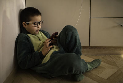 Closeup portrait of a boy who looks into the phone sitting on the floor, phone charging