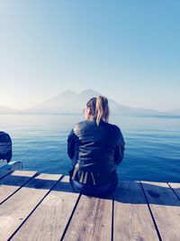 Woman sitting by sea against blue sky