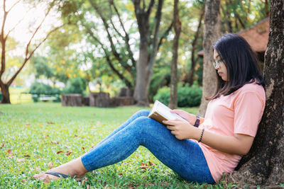 Side view of teenage girl reading book while sitting in public park
