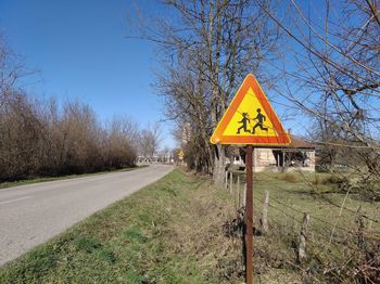 Road sign by trees against sky