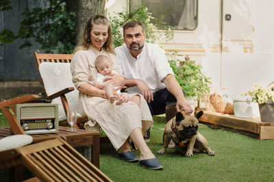 Family with baby and dog spending happy time together near trailer outside on deck chair, traveling