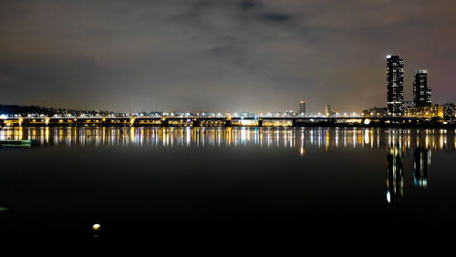 Illuminated buildings by sea against sky at night