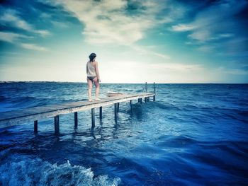 Rear view of man standing in sea against sky