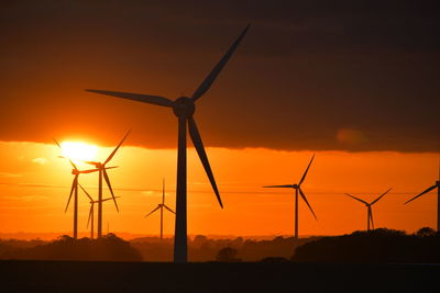 Silhouette wind turbines on field against sky during sunset