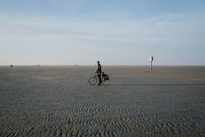 Man riding bicycle on sand against sky