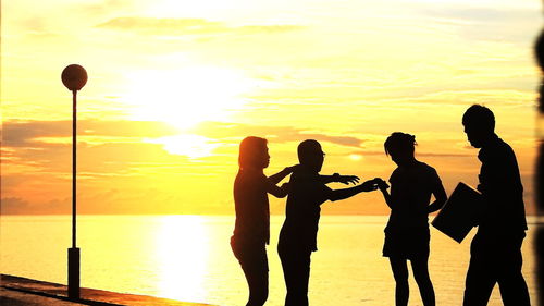 Silhouette friends standing on pier by sea against sky during sunset