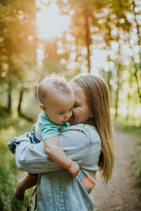 Vertical of happy mother snuggling baby boy outside in forest