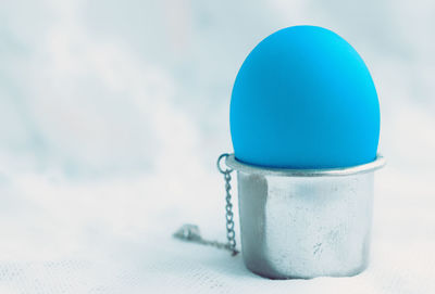 Blue egg in a silver eggcup close-up against blurred white tablecloth. selective focus, copy space.