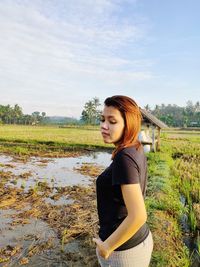 Young woman standing on field against sky