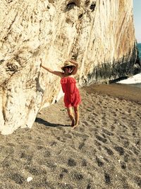 Young woman standing by rock formation at beach on sunny day