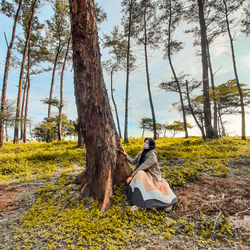 Woman sitting on tree trunk amidst plants