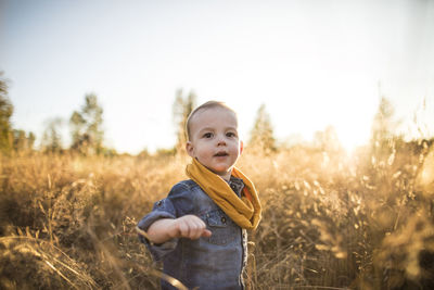 Cute baby boy standing on field against sky