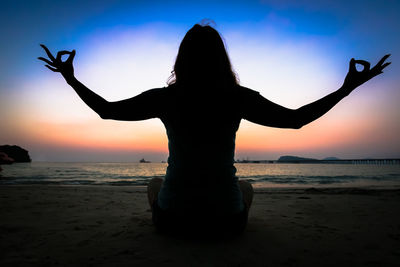 Rear view of silhouette woman standing at beach during sunset