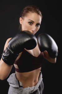 Portrait of young woman standing against black background